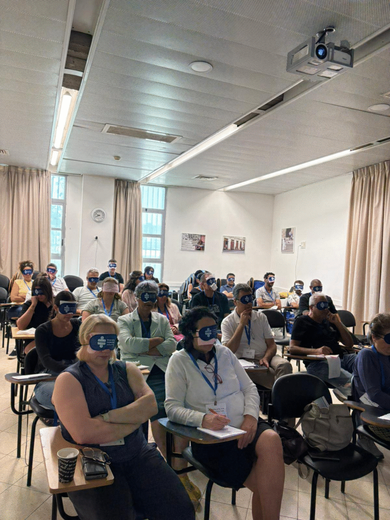המשתתפים ביום העיון מתנסים בתחנת מוגבלות בראייה ושמים כיסוי עיניים