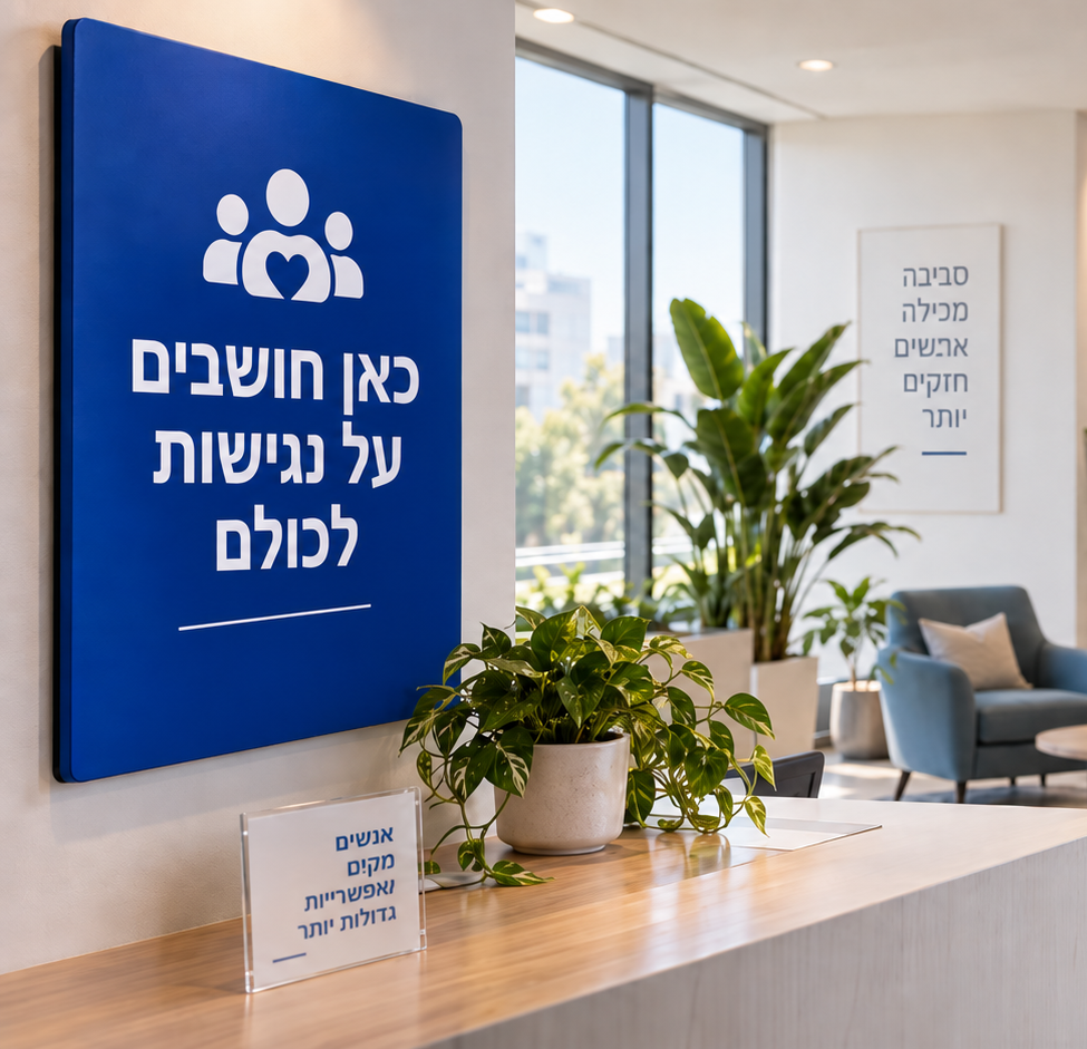 לובי משרדי מודרני ונגיש, עם שלט כחול שעליו הכיתוב "כאן חושבים על נגישות לכולם", פינת ישיבה, צמחייה ואישה בכיסא גלגלים במסדרון.