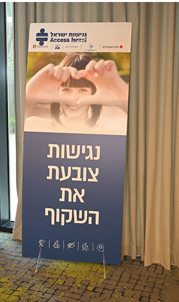 "שלט עומד של נגישות ישראל עם הכיתוב 'נגישות צובעת את השקוף'. בחלק העליון מופיעה אישה היוצרת צורת לב עם ידיה, וברקע לוגו נגישות ישראל."